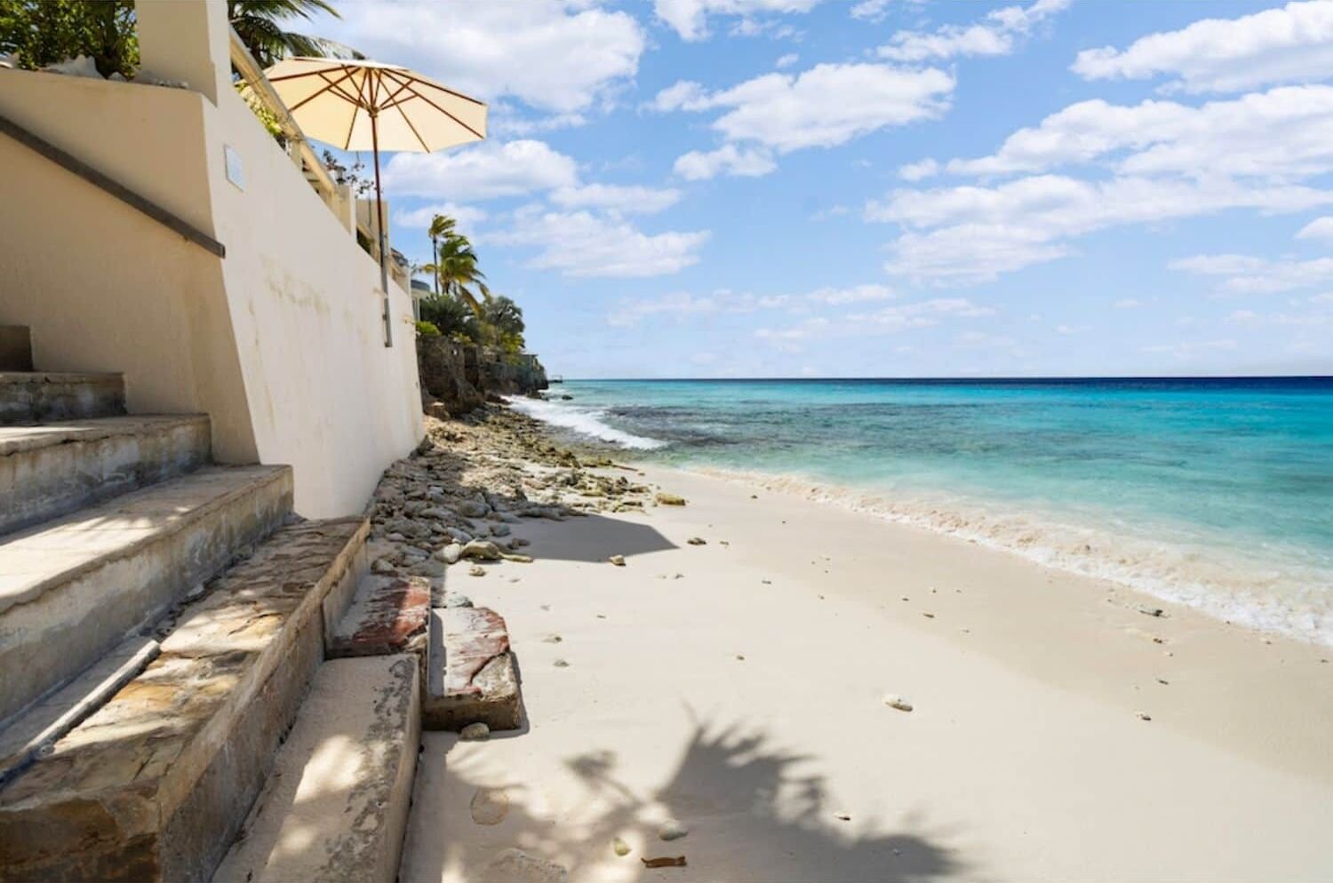 A beach with steps leading down to the shore, a palm tree, and a clear blue sky.