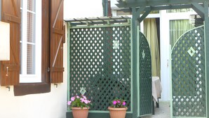 A wooden gate with lattice design, two potted plants with pink flowers, and a concrete pathway. - Apartment 'L'Appartement Du Moulin' with Private Terrace and Wi-Fi (Mascaras)