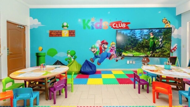 Um espaço infantil com móveis coloridos, uma televisão grande e decoração temática do Mario.