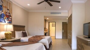 Quarto de hotel com duas camas, um ventilador de teto, uma televisão e um objeto decorativo na parede.