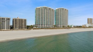 Een hotel aan het strand met meerdere hoge gebouwen, een zandstrand en helderblauw water.