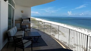 Een balkon met een barbecue, zitplaatsen en uitzicht op het strand.