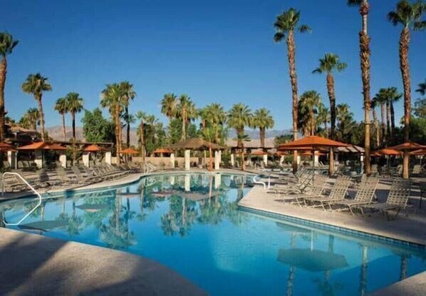 A pool area with lounge chairs and umbrellas, surrounded by palm trees. - Marriott Desert Springs Villas II Resort - Perfect for Coachella 2026 (Palm Desert)