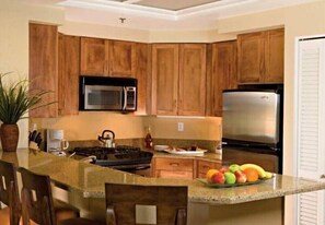 A kitchen with wooden cabinets, a stainless steel refrigerator, a microwave, and a granite countertop. - Marriott Desert Springs Villas II Resort - Perfect for Coachella 2026 (Palm Desert)