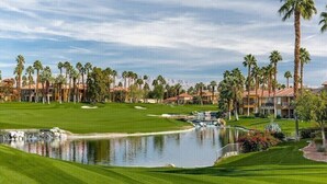 Un campo de golf con un estanque, palmeras y un edificio con techo rojo.