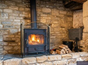 A stone fireplace with a black stove, logs, and a basket.