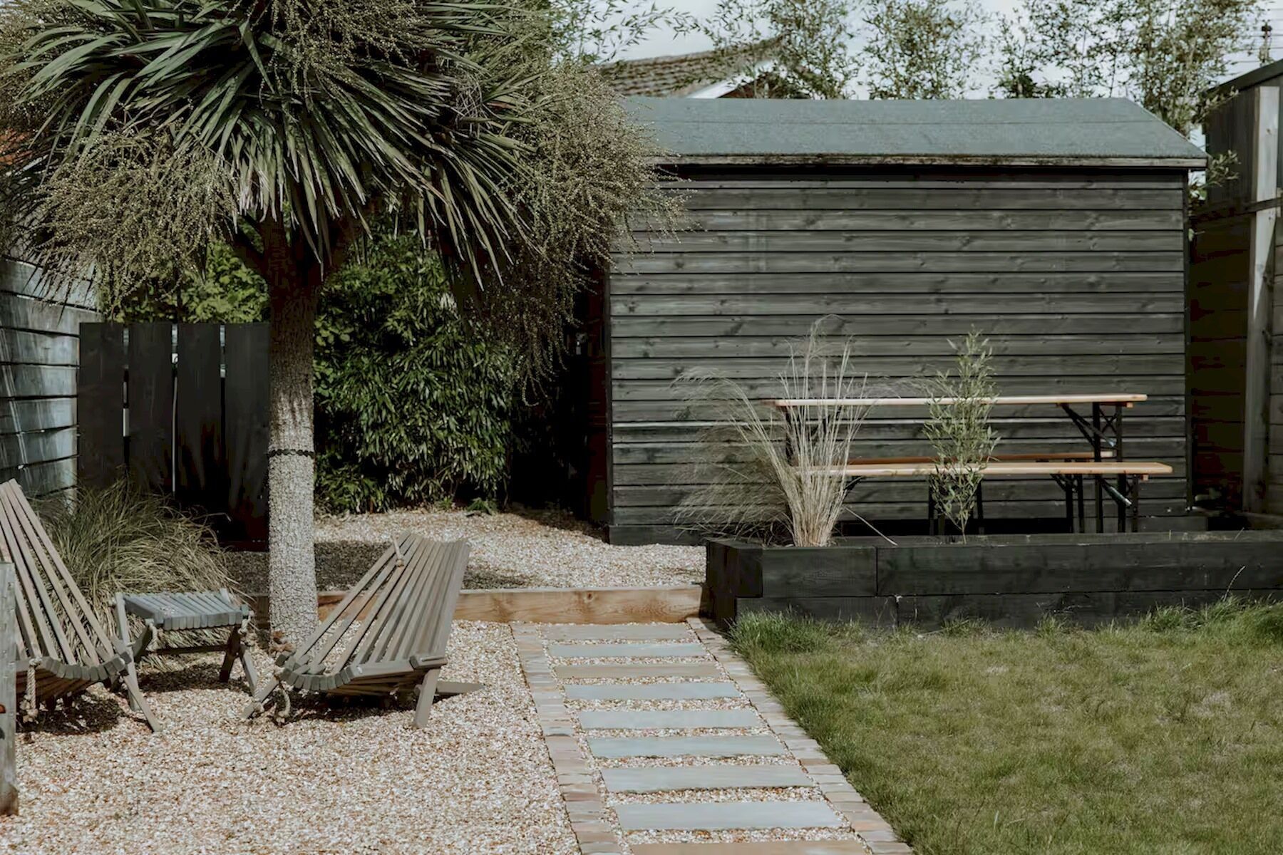 Un patio con un banco de madera, una mesita y una palmera.