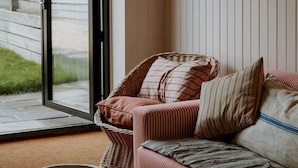 Ein gemütlicher Raum mit einem Korbstuhl, einem gestreiften Sofa und einer Schale auf dem Boden.