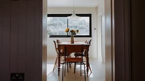 Ein Essbereich mit Holztisch und Stühlen, einer Blumenvase und Blick auf eine verschneite Landschaft durch ein großes Fenster.