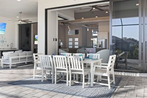A modern outdoor dining area with white furniture, a ceiling fan, and a view of the backyard. - Southern Sun - New Listing! (Cape Coral)