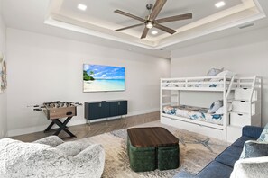 A modern living room with a foosball table, a sofa, a coffee table, a bunk bed, and a ceiling fan. - Southern Sun - New Listing! (Cape Coral)