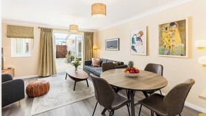 Un salon moderne avec un coin repas, comprenant une table ronde en bois, des fauteuils en cuir, un canapé et des œuvres d’art accrochées aux murs.