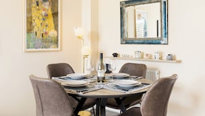 Un coin repas avec une table ronde dressée pour quatre personnes, une bouteille de vin et un tableau encadré accroché au mur.