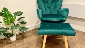 A teal upholstered chair with wooden legs and a matching ottoman, placed on a wooden floor against a white wall. - Converted Ancoats Mill - Walk to Victoria - Pass the Keys (Manchester)