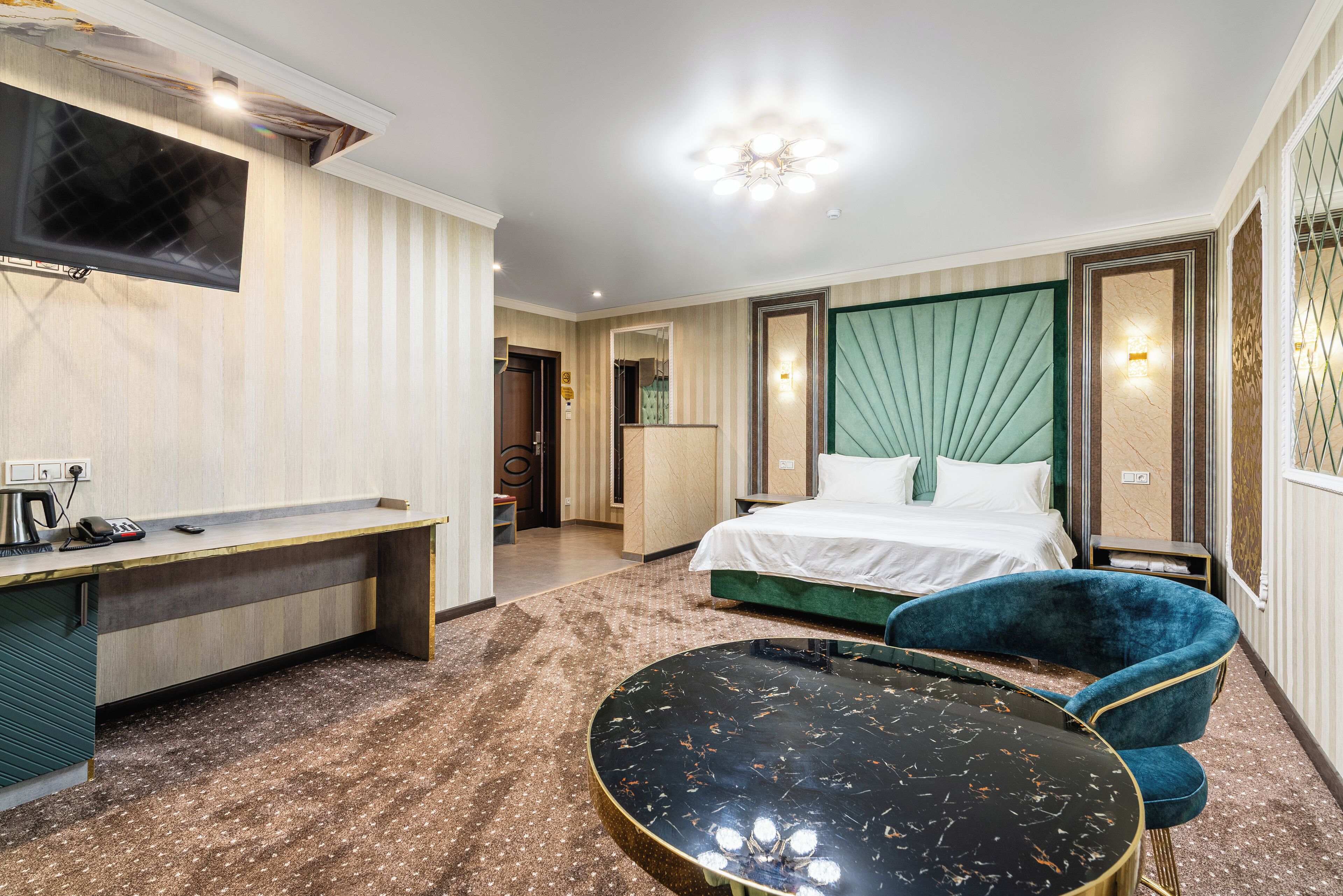 A hotel room with a bed, a desk, a chair, a round table, and a TV.