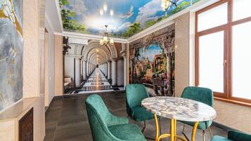 Un vestíbulo con sillas tapizadas de verde, una mesa de mármol y un mural que representa un paisaje urbano.