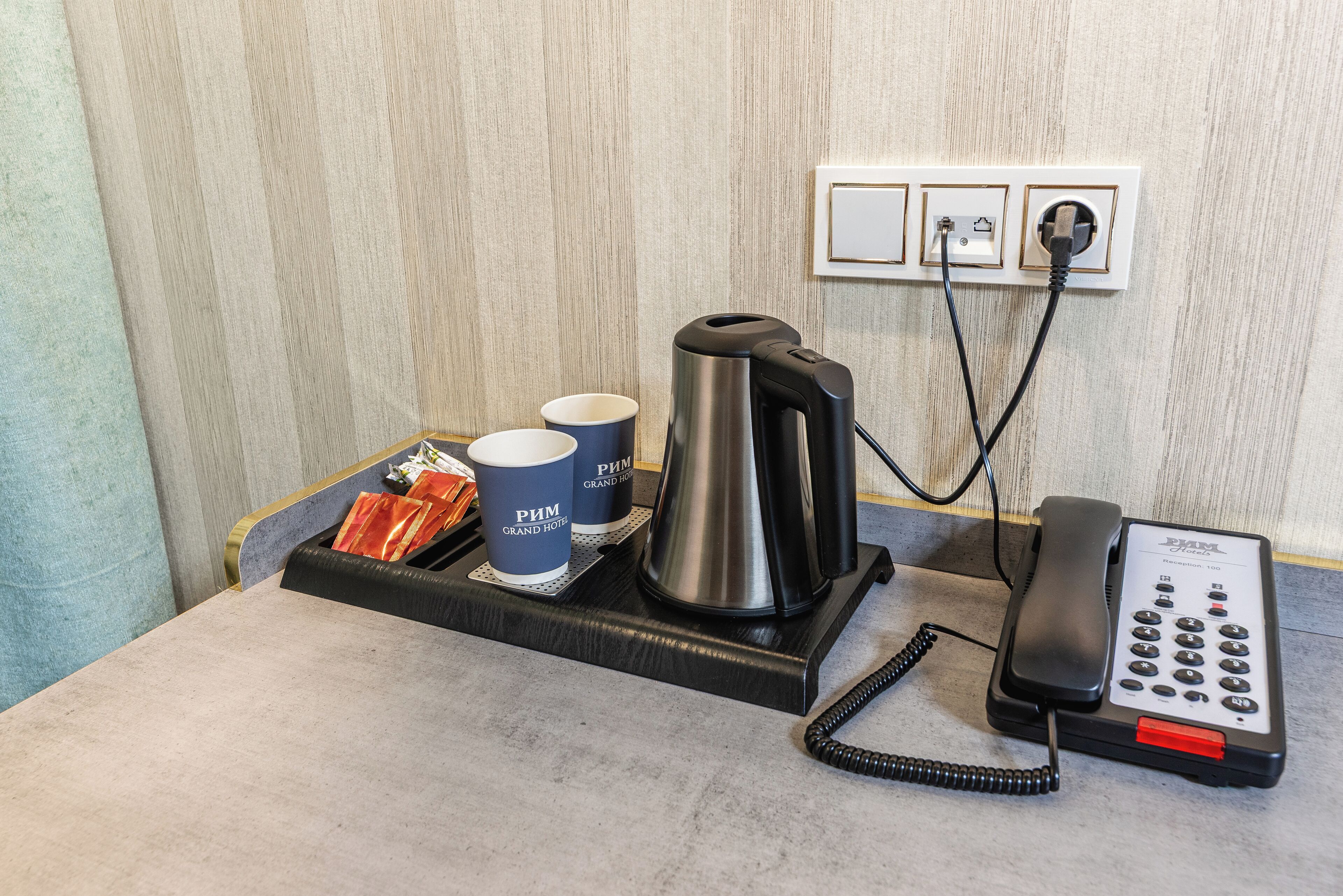 A hotel room with a coffee maker, two cups, a phone, and a tray with snacks.