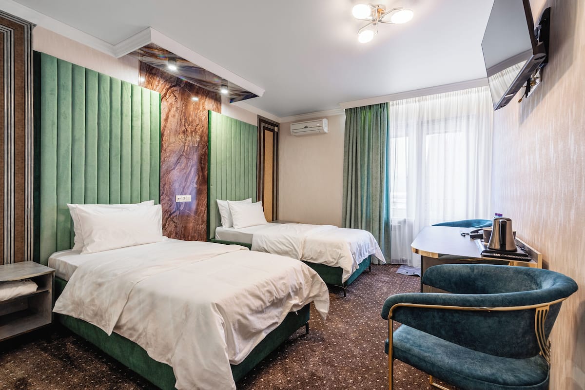 Una habitación de hotel con dos camas, un escritorio, una silla y un televisor montado en la pared.