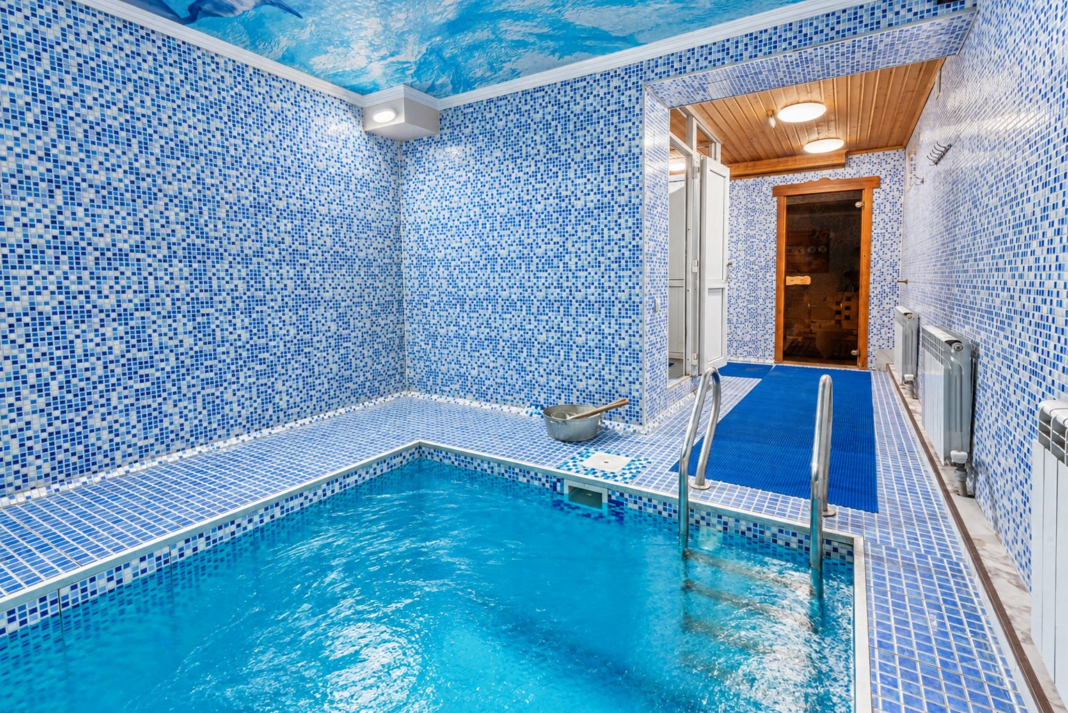 Ein Innenpool mit blauen Mosaikfliesen, einem Sprungbrett und einer Holzbalkendecke.