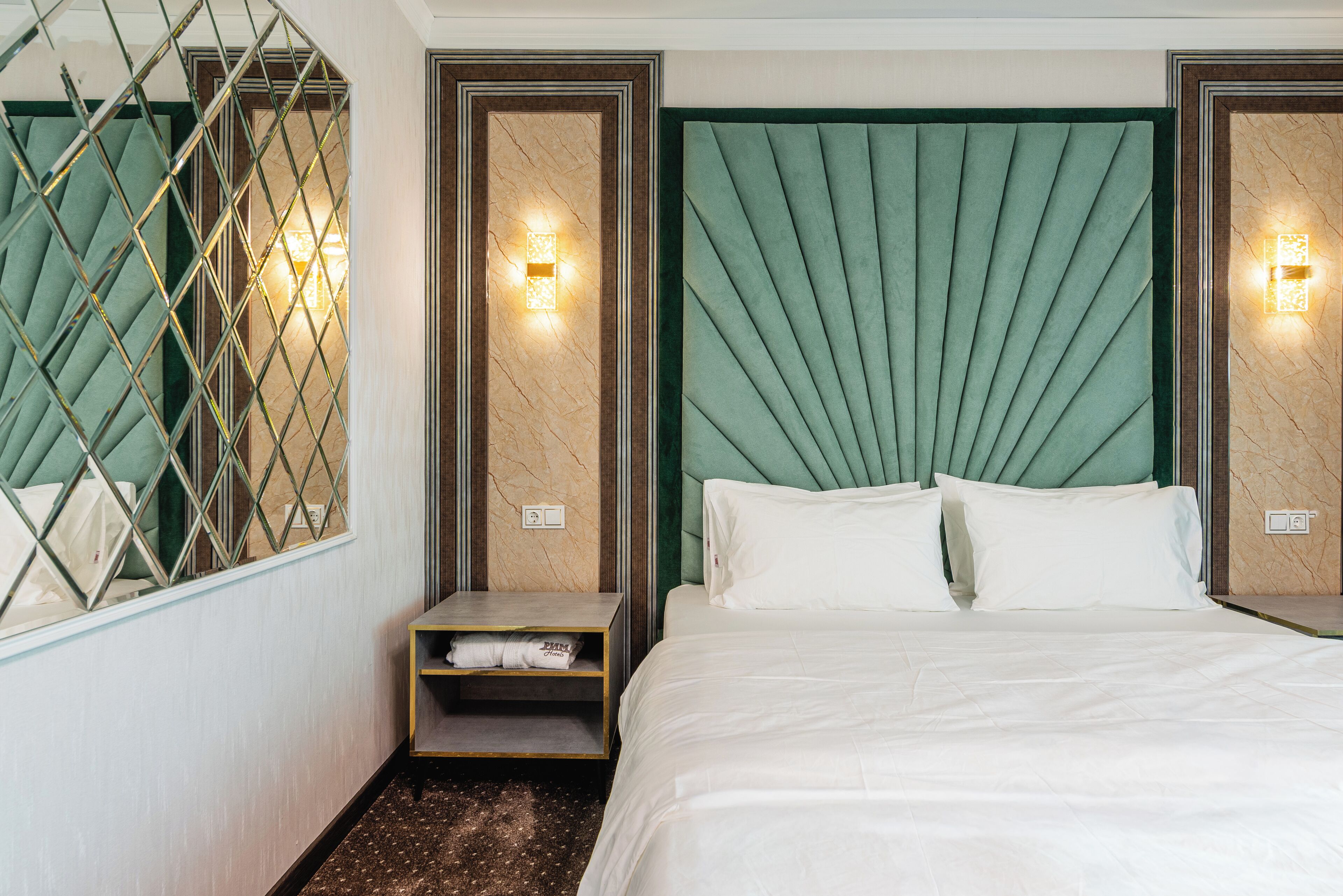 A hotel room with a large bed, two bedside tables, a mirror, and a decorative wall panel.