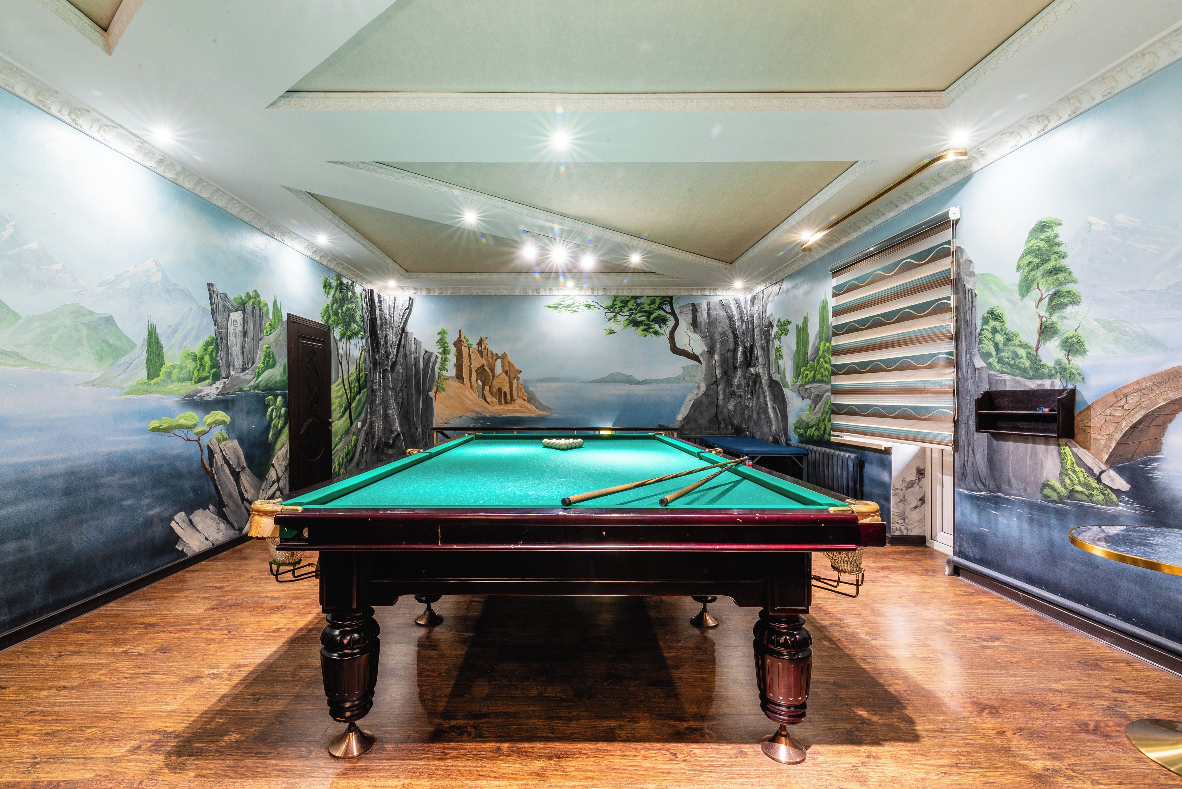 A pool table in a room with a mural of a mountainous landscape on the walls.