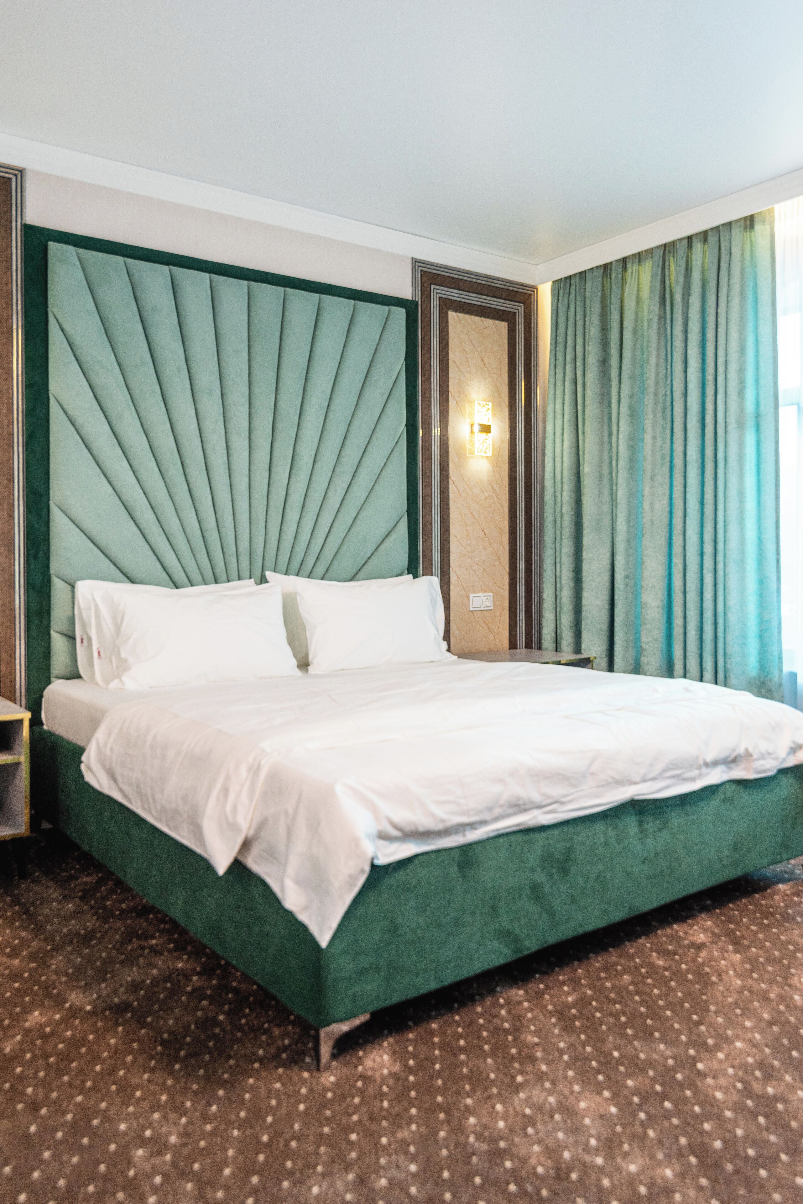 Une chambre d’hôtel avec un grand lit, une tête de lit recouverte d’un tissu vert et un mur décoratif en marbre.