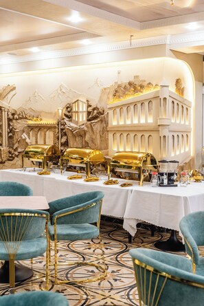 A luxurious dining area with gold buffet stations, teal chairs, and a decorative wall mural.