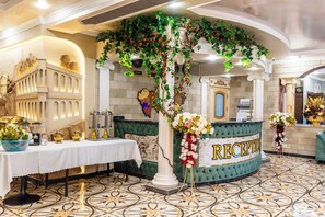 A reception area with a green reception desk, white columns, and a tiled floor.