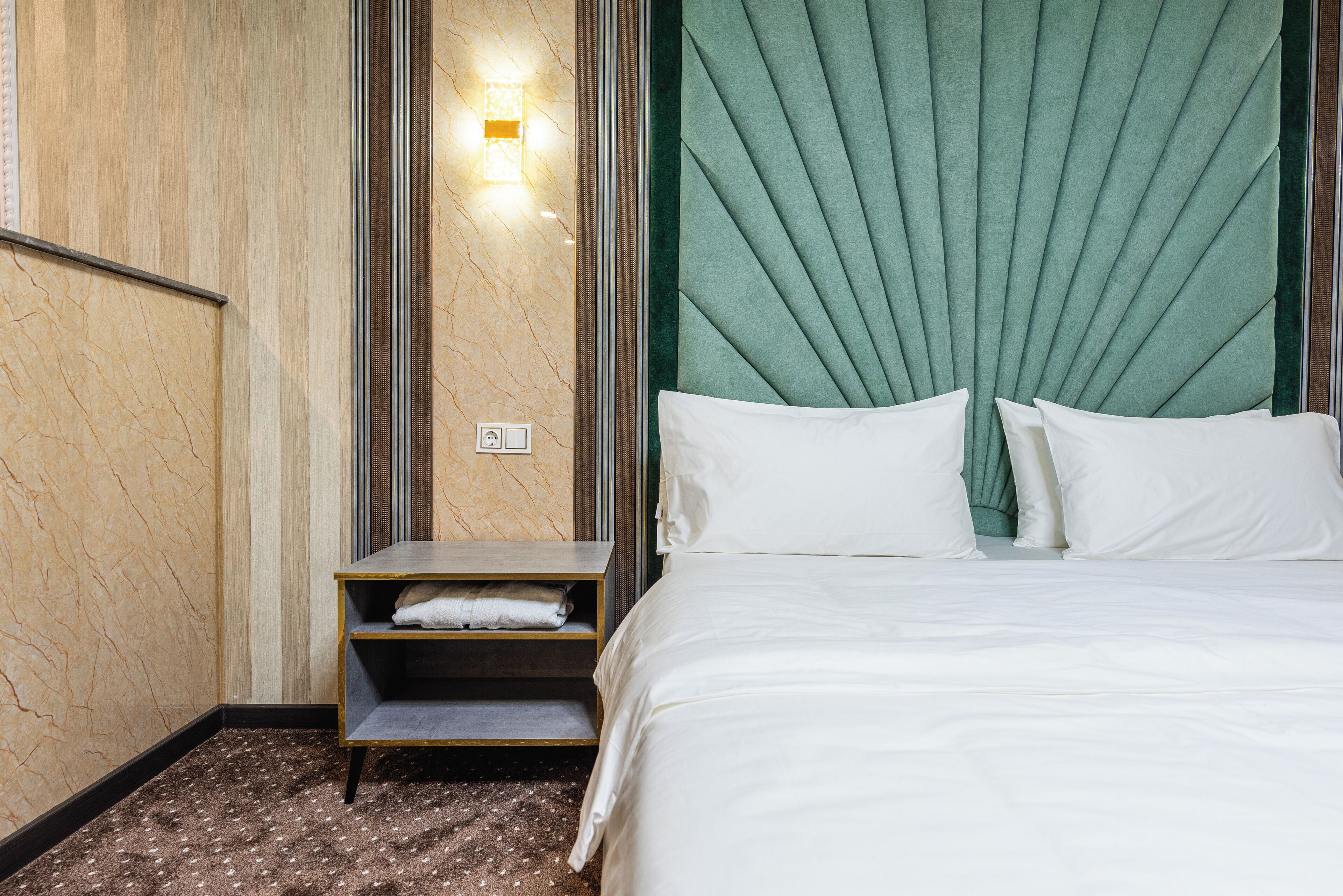 A hotel room with a bed, a nightstand, a wall-mounted light, and a marble-patterned wall.