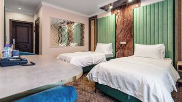 Habitación de hotel con dos camas individuales, una mesita con un teléfono y una ventana con un panel decorativo.
