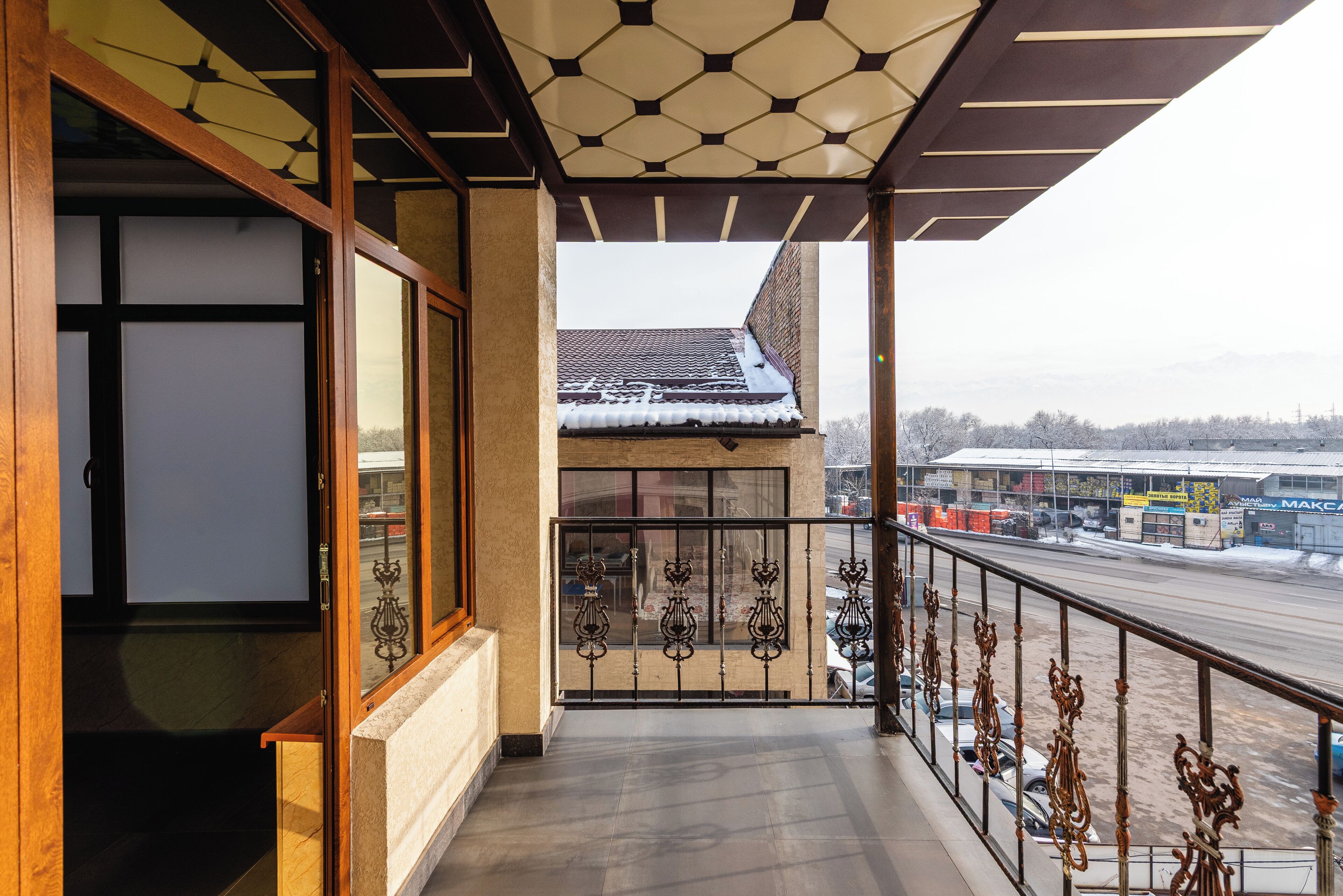 A balcony with a metal railing, a view of a snowy street, and a building with a tiled roof.