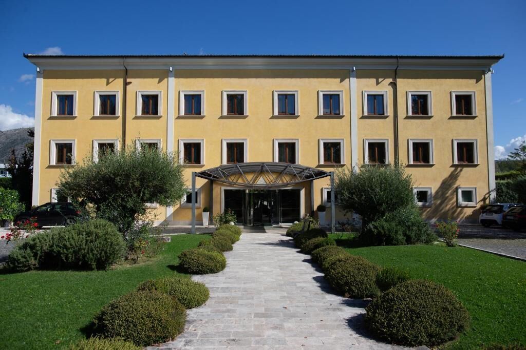 A yellow building with a central entrance, surrounded by well-maintained hedges and a clear sky.