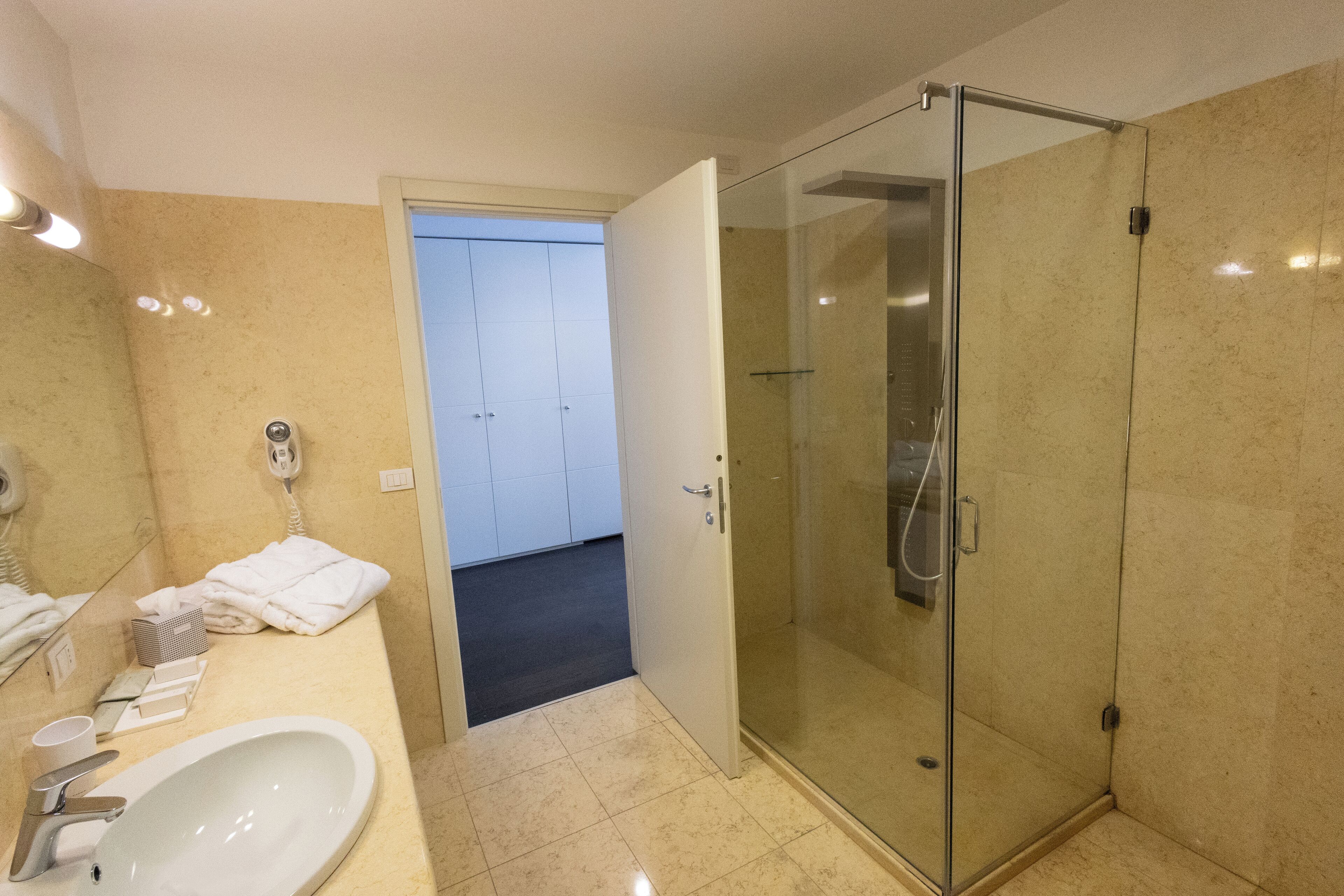 A modern bathroom with a glass-enclosed shower, a sink with a mirror, and a door leading to another room.
