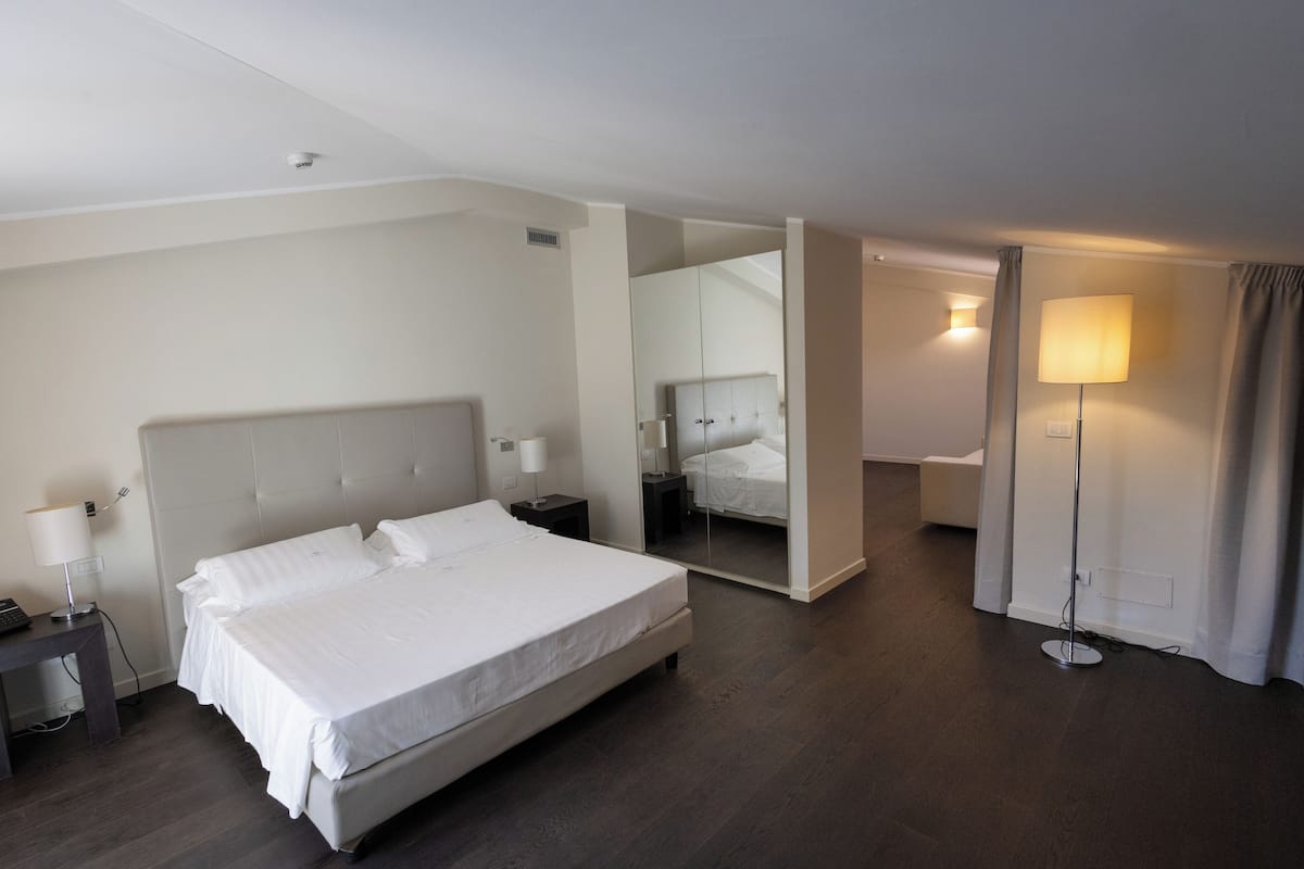 Moderni hotellihuone, jossa on suuri sänky, yöpöydät, peili, lattiavalaisin ja vaatekaappi.