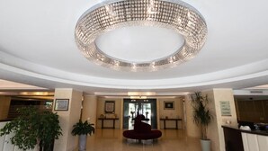 A spacious lobby with a large circular chandelier, a reception desk, and potted plants. - Hotel La Dimora del Baco (L'Aquila)