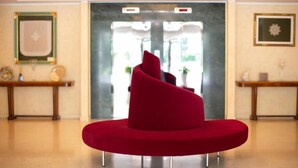 A red chair in a lobby with a marble floor, a reception desk, and framed artwork on the walls. - Hotel La Dimora del Baco (L'Aquila)