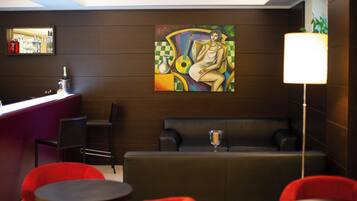 Un moderno vestíbulo de hotel con zona de bar, sillas rojas, un sofá y un cuadro abstracto de gran tamaño en la pared.