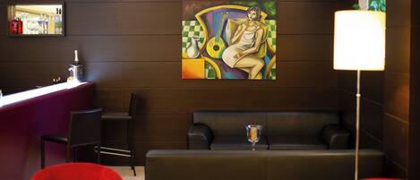 A modern hotel lobby with a bar area, red chairs, a sofa, and a large abstract painting on the wall.