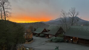 Un chalet doté de plusieurs cabanes, d’un espace de stationnement et surplombant un paysage montagneux au coucher du soleil.