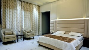 A hotel room with a large bed, two armchairs, a small table, and a decorative vase. - Florentino The Luxury Villa (Amritsar)