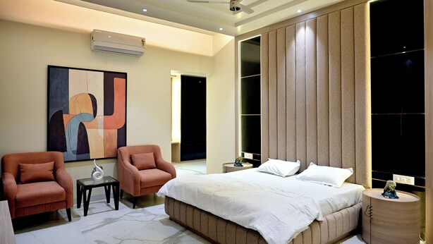 A modern bedroom with a large bed, two armchairs, a side table, and a ceiling fan. - Florentino The Luxury Villa (Amritsar)