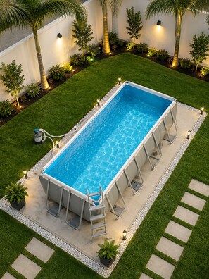 Una piscina rectangular con una escalera, rodeada por un borde de grava blanca y un césped verde.