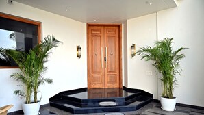 A modern entrance with a wooden door, two potted plants, and a black and grey tiled floor. - Florentino The Luxury Villa (Amritsar)