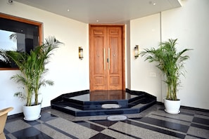 Una entrada moderna con puerta de madera, dos plantas en macetas y suelo de baldosas negras y grises.