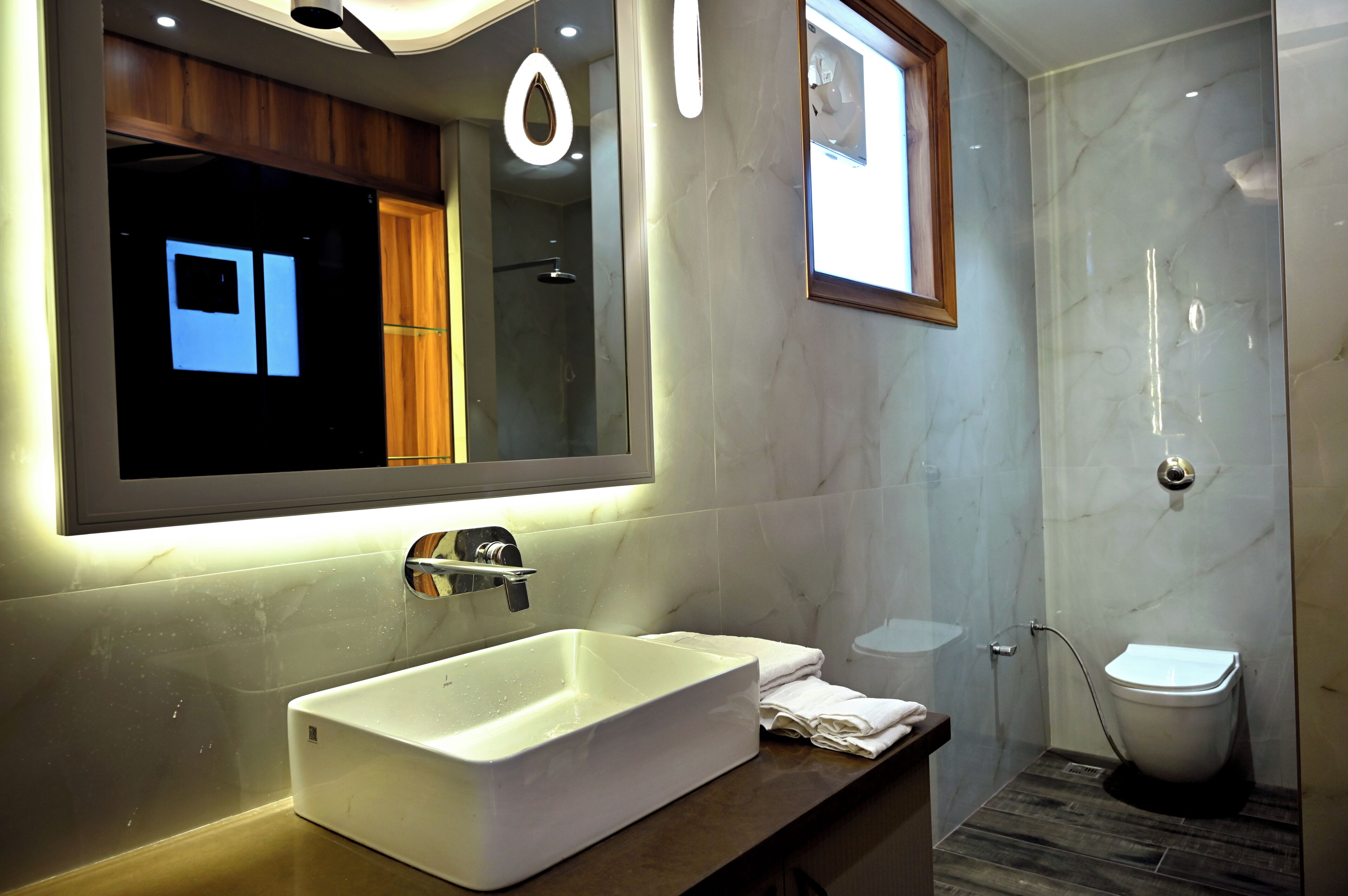 A modern bathroom with a large mirror, a rectangular sink, a toilet, and a shower area.