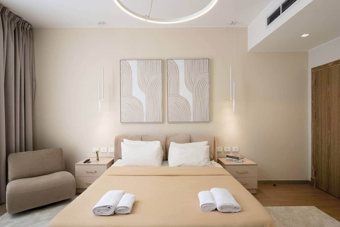 Una habitación de hotel moderna con una cama, dos mesitas de noche, una silla y arte abstracto en la pared.