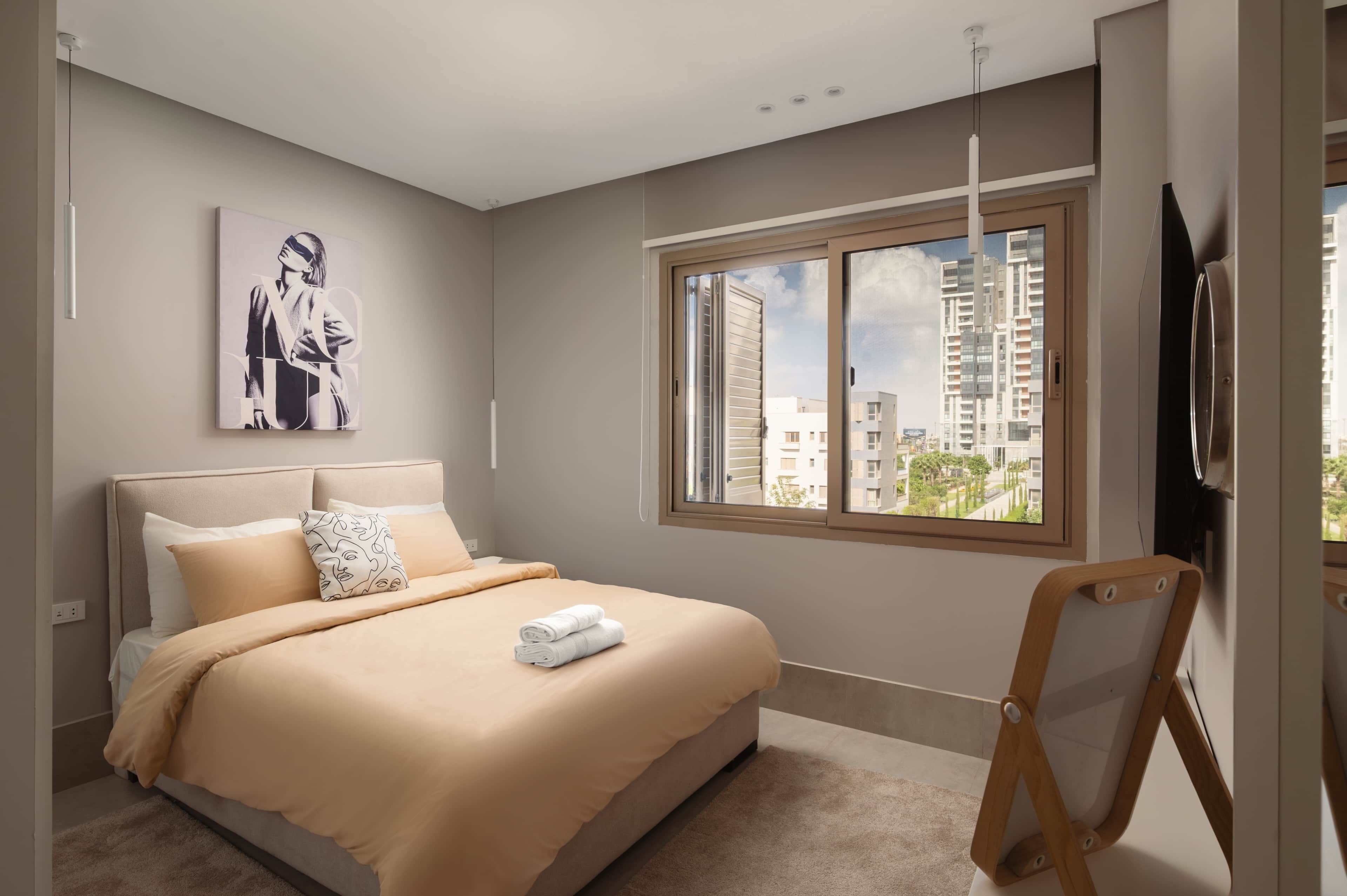 Ein Schlafzimmer mit einem Bett, einem Fenster mit Blick auf die Stadt, einem Gemälde an der Wand und einem Fernseher.