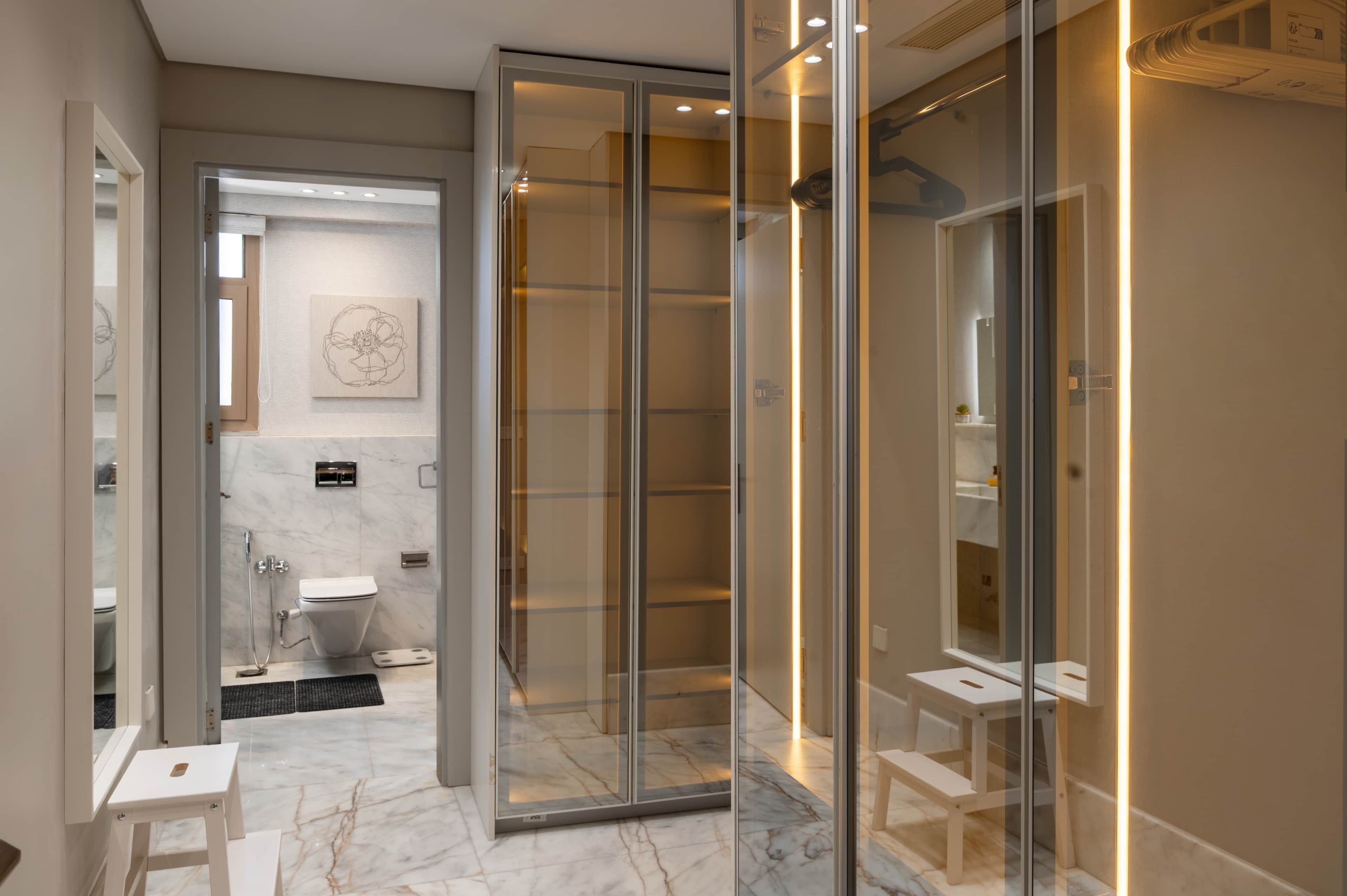 A modern bathroom with a glass shower enclosure, a marble floor, and a small white stool.