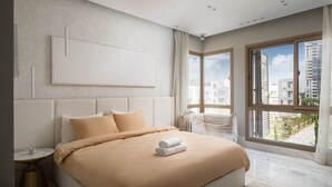 Ein modernes Schlafzimmer mit einem großen Bett, einem Nachttisch, einem Wandbild und Blick auf die Stadt durch große Fenster.