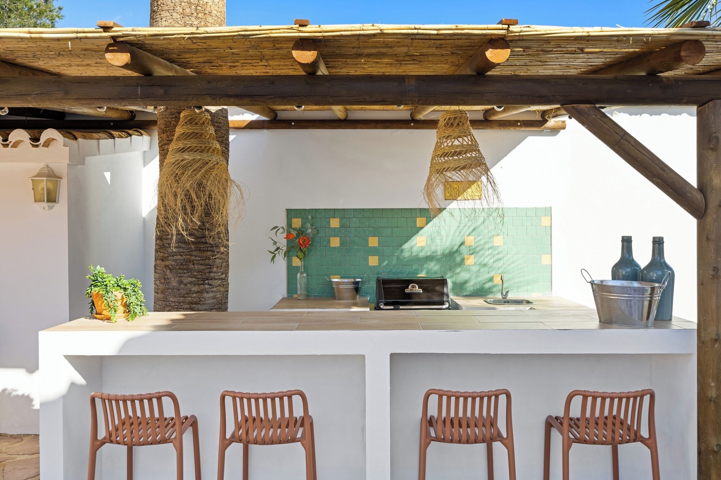 Una cocina exterior con encimera blanca, una parrilla y dos taburetes de bar.